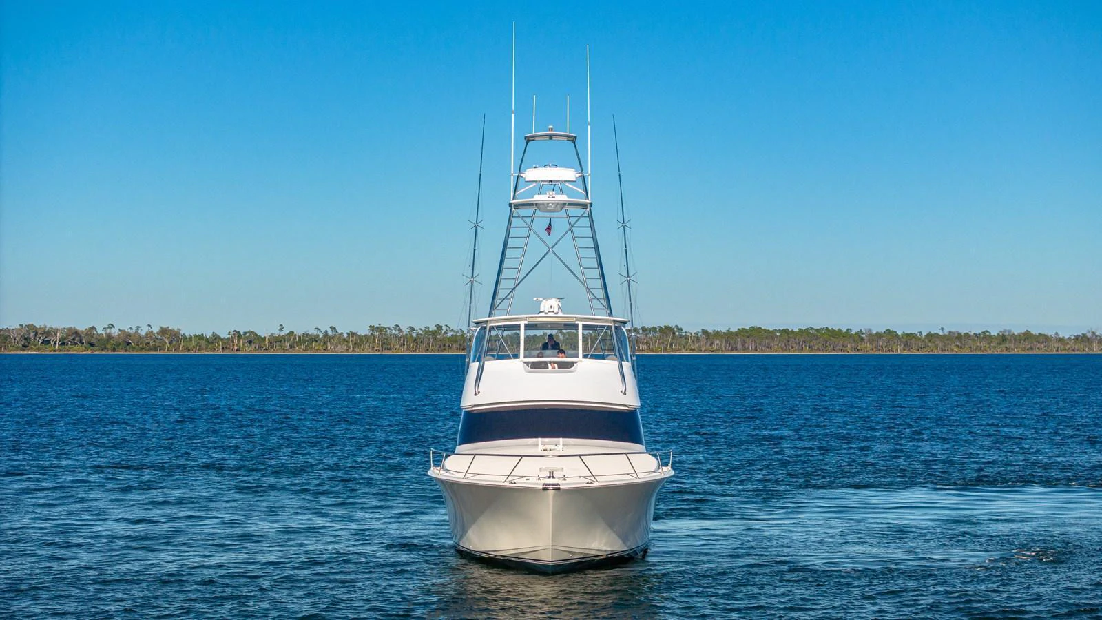 A sleek yacht is seen head-on, cruising on calm waters with a clear blue sky in the background. aboard FIRST BITE Yacht for Sale