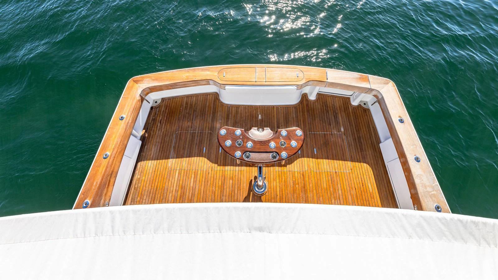 The aft deck features a polished wooden floor with a central fishing station, overlooking the serene water. aboard FIRST BITE Yacht for Sale