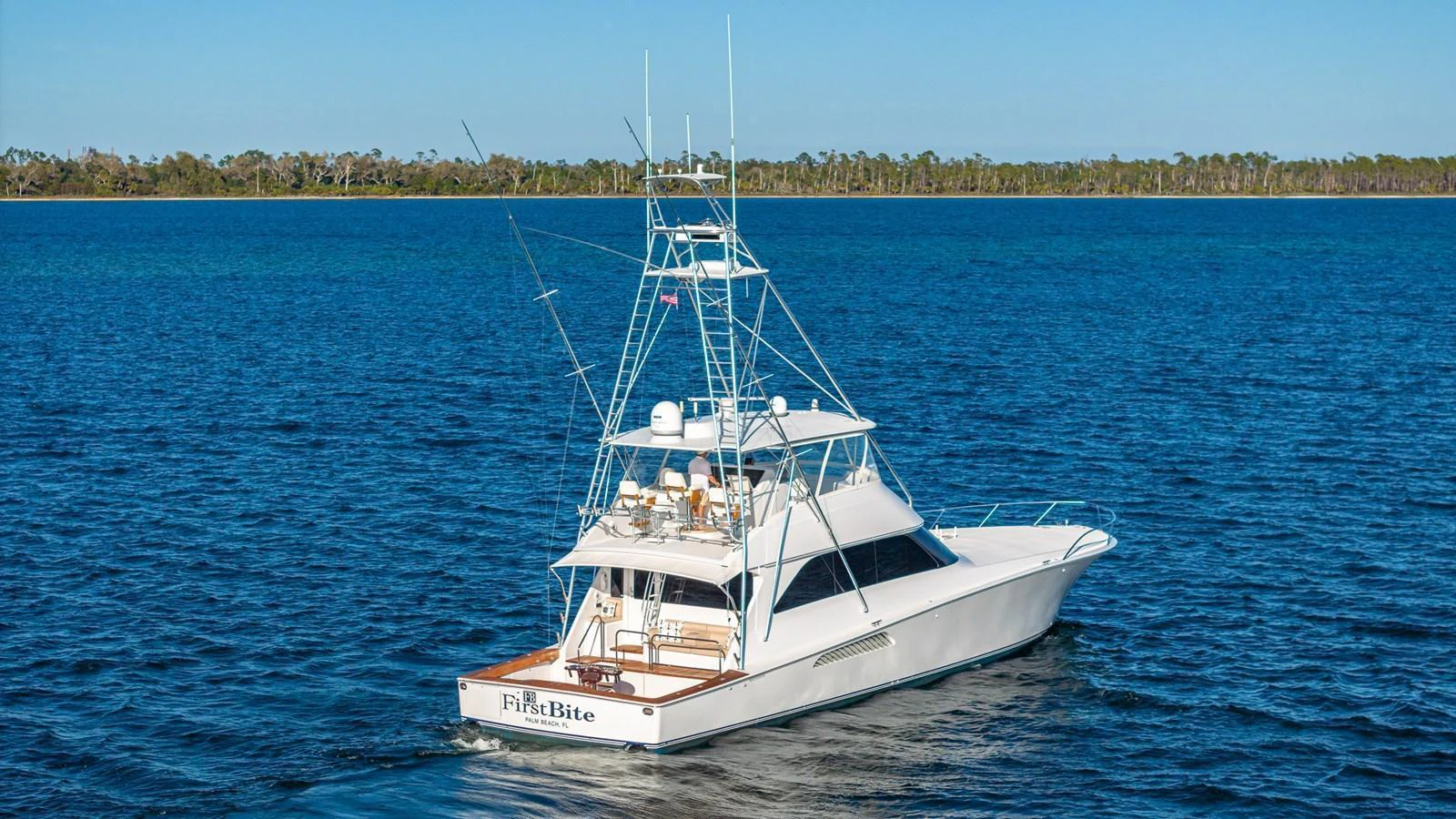 A sleek yacht cruises on calm blue waters with a scenic shoreline in the background. aboard FIRST BITE Yacht for Sale