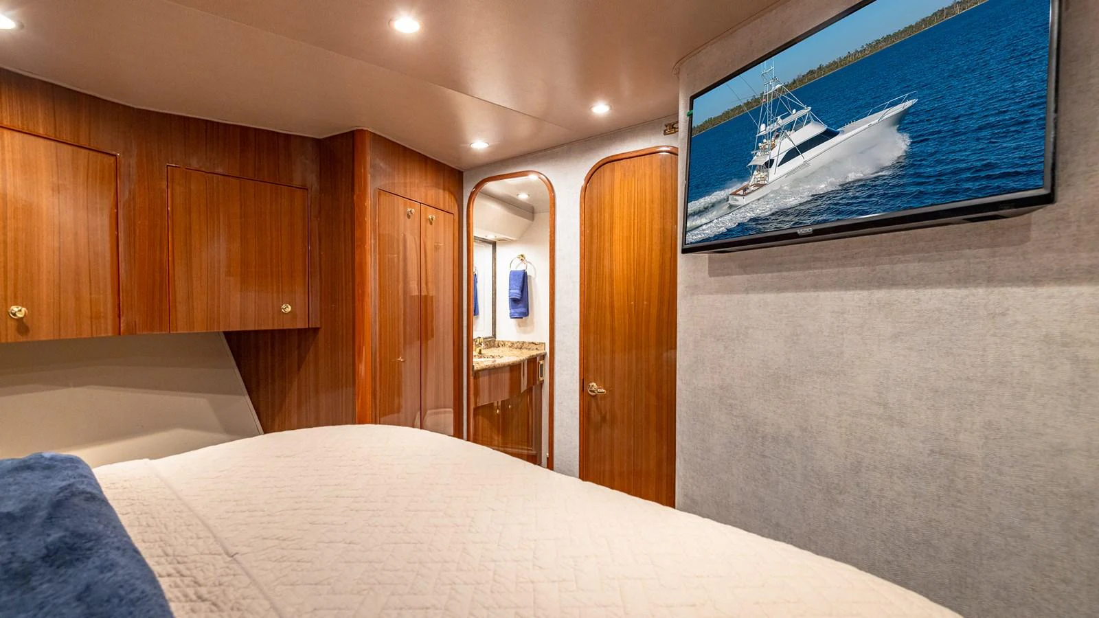 The stateroom features warm wood finishes, a comfortable bed, and a mounted TV displaying a yacht on the water. aboard FIRST BITE Yacht for Sale