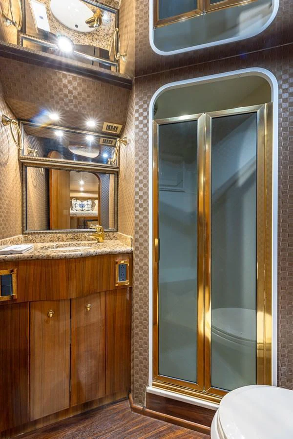 The yacht's bathroom features elegant wood cabinetry, a granite countertop, and a glass shower enclosure with gold accents. aboard FIRST BITE Yacht for Sale