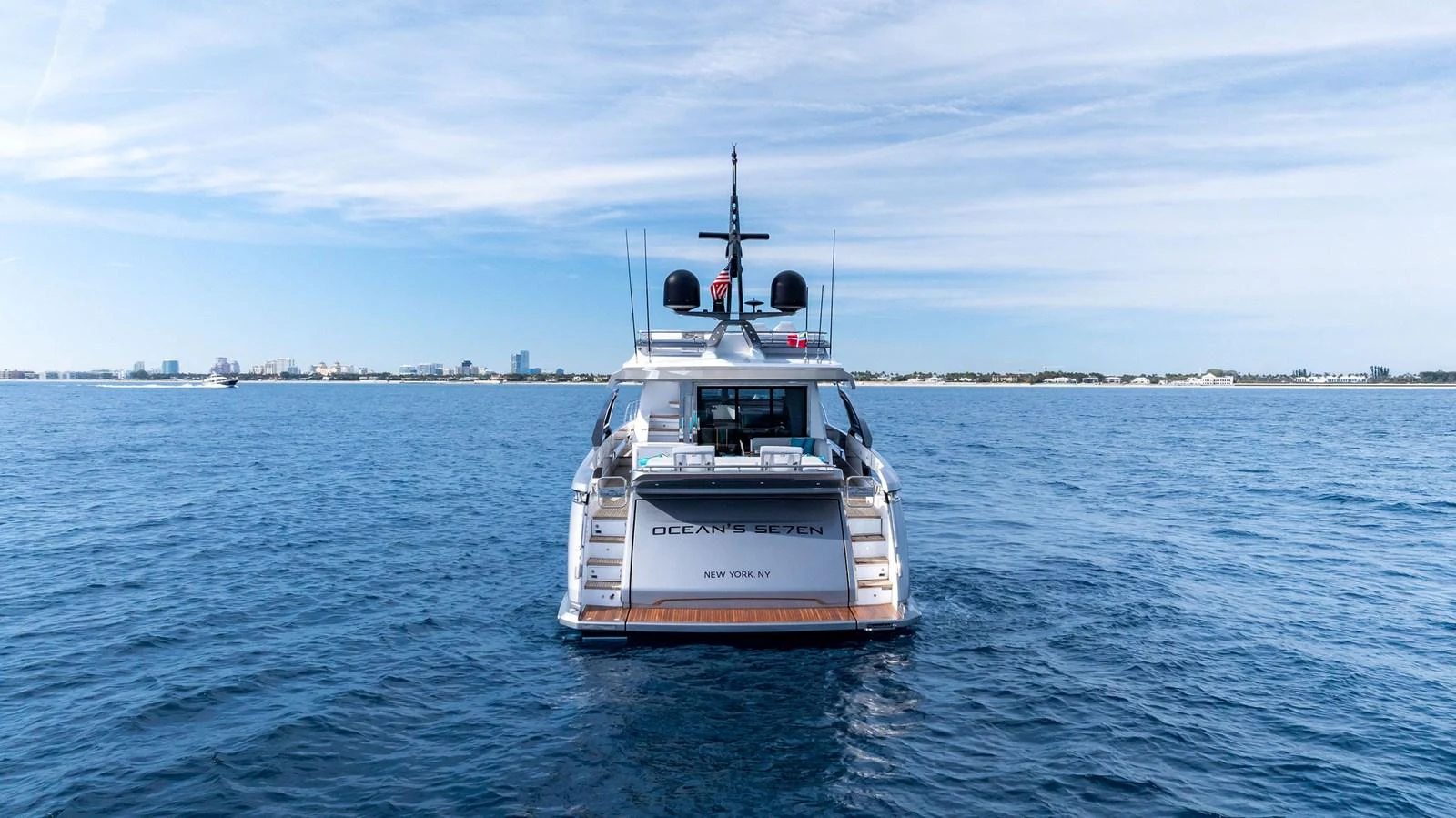 A sleek yacht is seen from the rear, cruising on calm blue waters under a clear sky. aboard OCEAN'S SE7EN Yacht for Sale