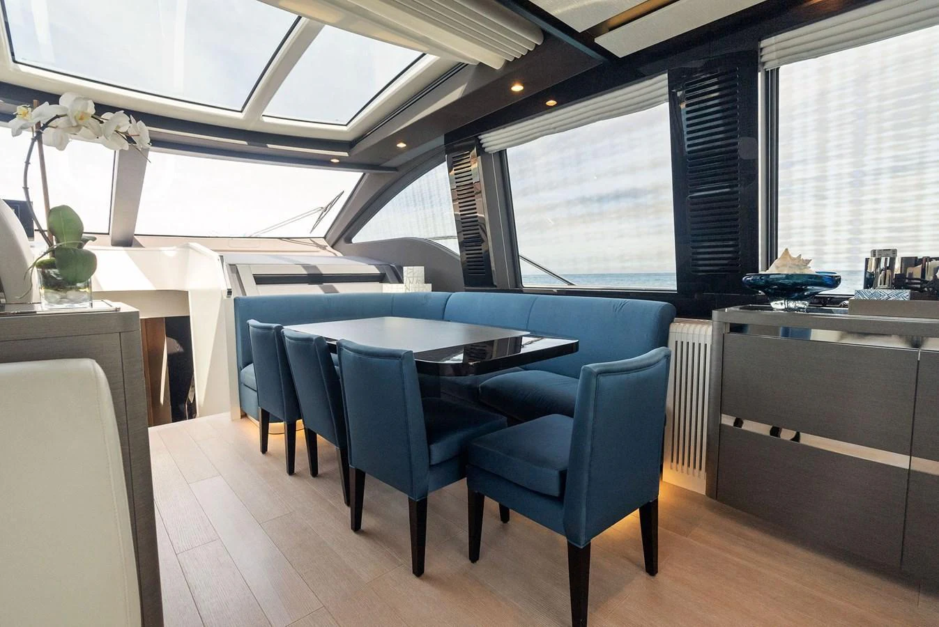 The yacht's dining area features a sleek table surrounded by plush blue chairs, set against large windows that offer stunning views. aboard OCEAN'S SE7EN Yacht for Sale