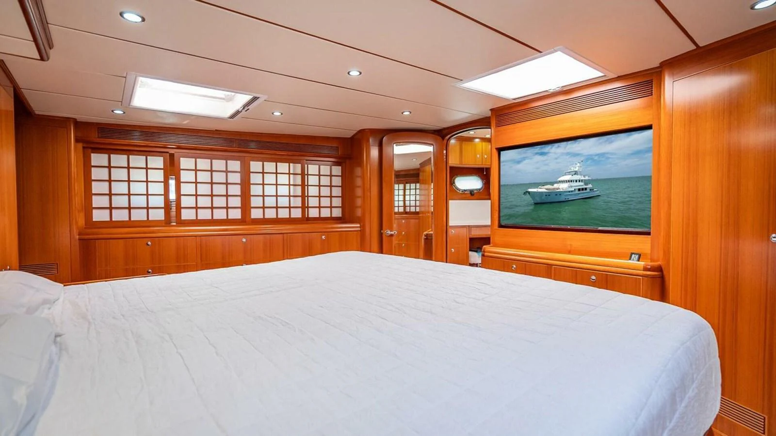 The master stateroom features a spacious bed, warm wood finishes, and a large screen displaying a serene ocean scene. aboard TAKE 5 Yacht for Sale
