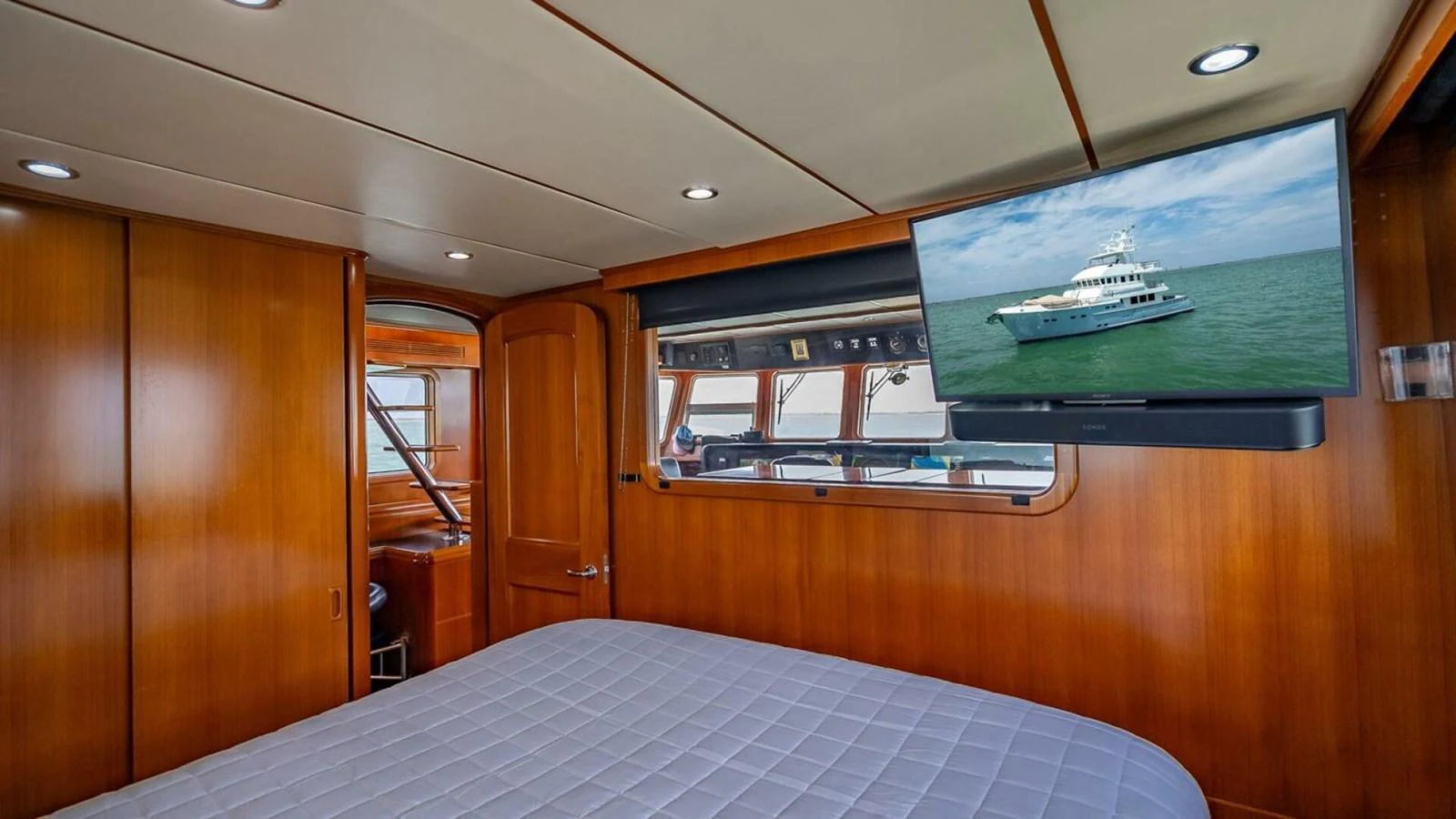 A cozy stateroom with a large bed and a mounted TV displaying an exterior view of a yacht. aboard TAKE 5 Yacht for Sale