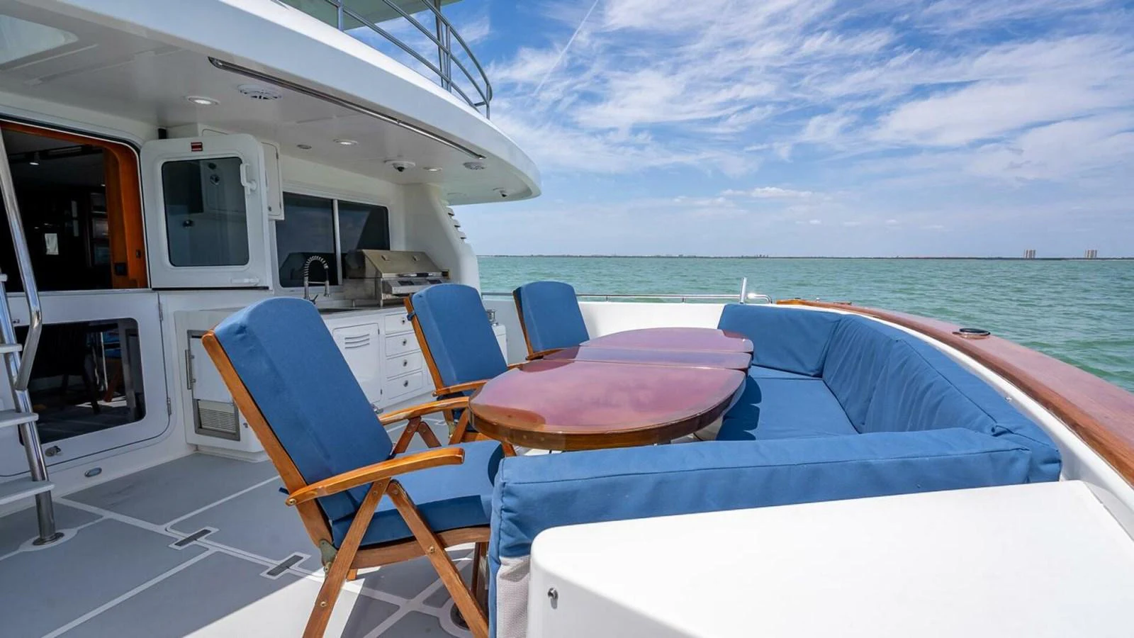 The aft deck features a comfortable seating area with blue cushions and a wooden table, perfect for enjoying the sea view. aboard TAKE 5 Yacht for Sale