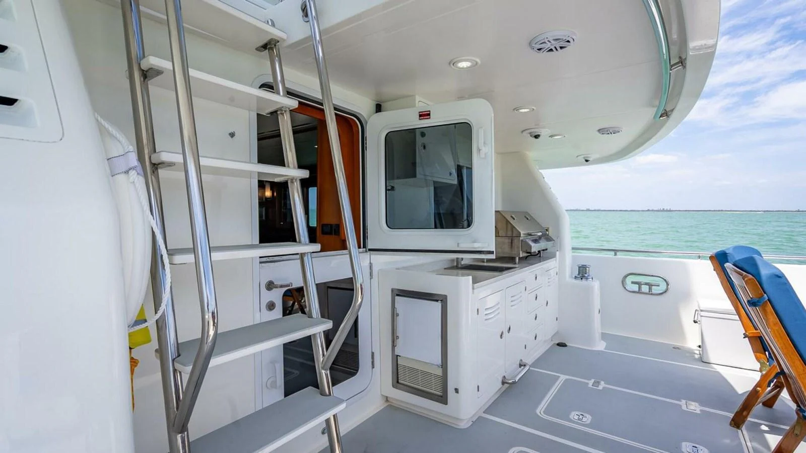 The aft deck features a compact outdoor kitchen and a ladder leading to the upper deck, with a serene ocean view in the background. aboard TAKE 5 Yacht for Sale