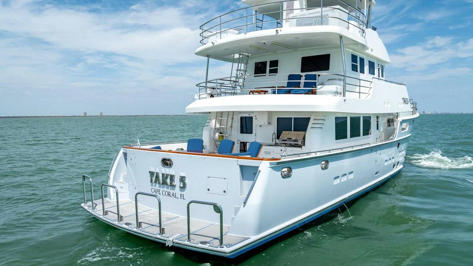 A luxurious yacht cruising on calm waters with a spacious aft deck and multiple levels of outdoor seating. aboard TAKE 5 Yacht for Sale