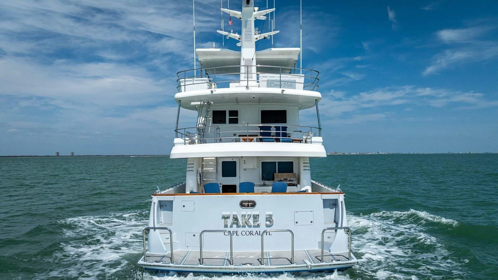 The yacht is seen cruising on the water, showcasing its stern with a clear view of the multiple decks and open sea behind. aboard TAKE 5 Yacht for Sale
