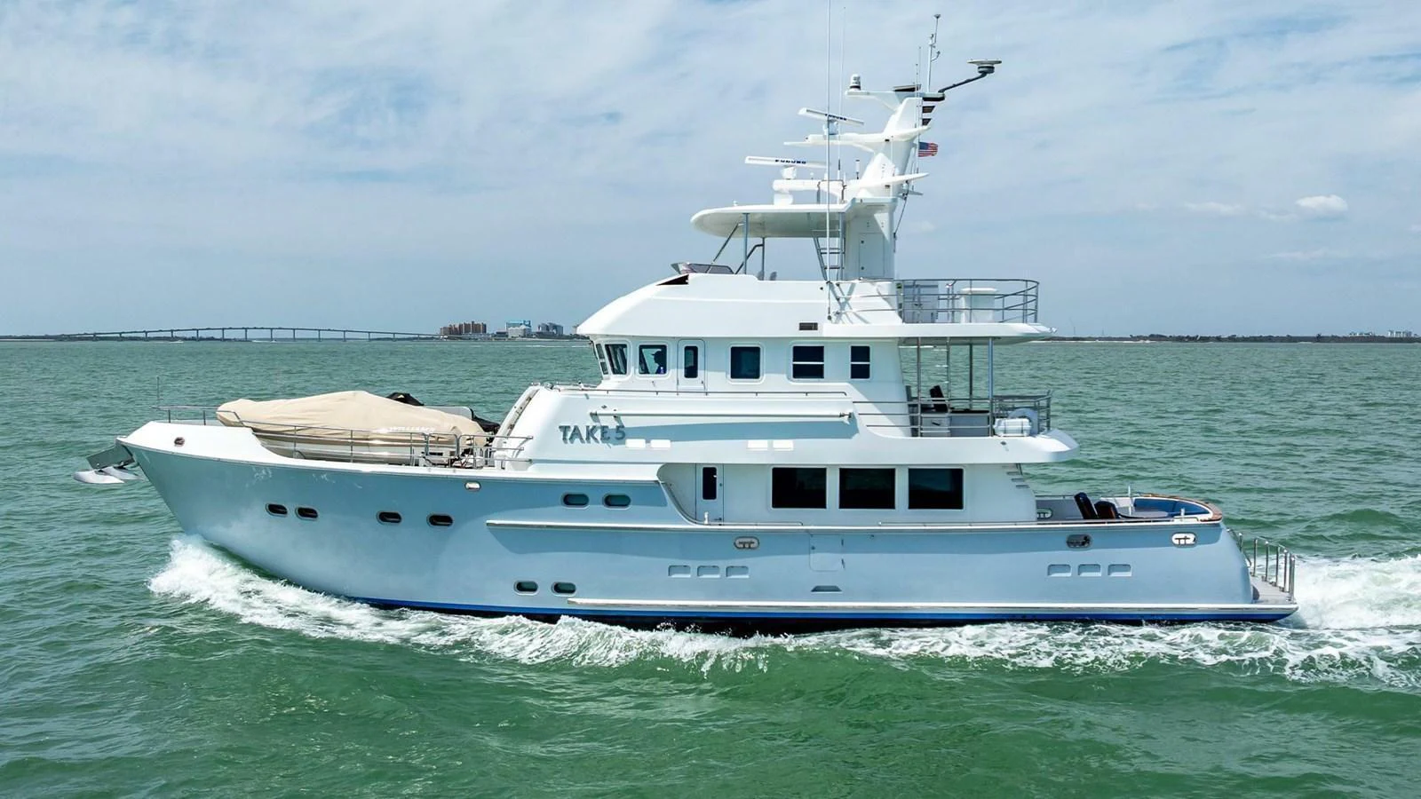 A sleek white yacht cruises through calm waters under a clear sky. aboard TAKE 5 Yacht for Sale