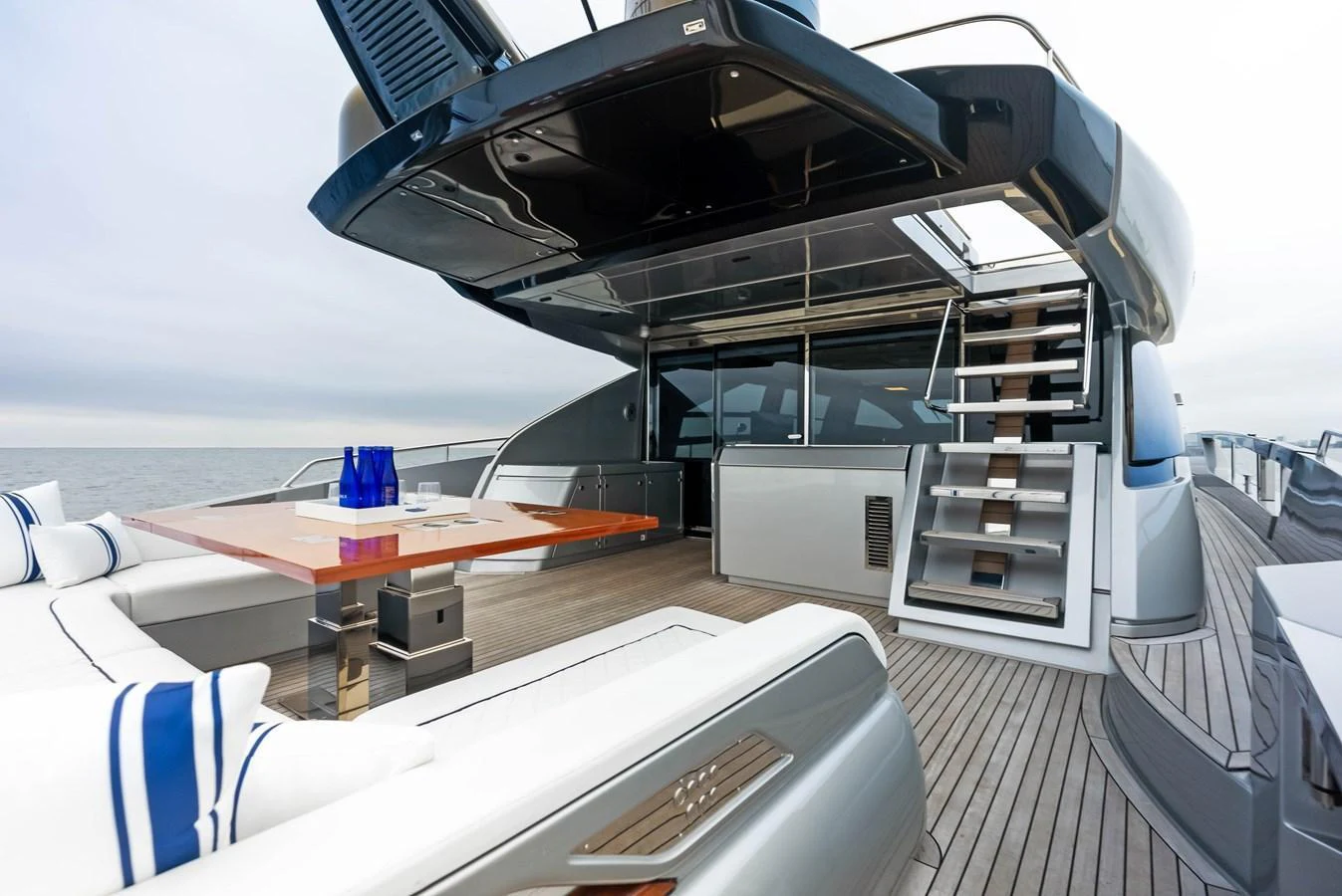The aft deck features a stylish seating area with a sleek dining table and modern staircase leading to the upper deck. aboard FERRETTI  TRADE Yacht for Sale