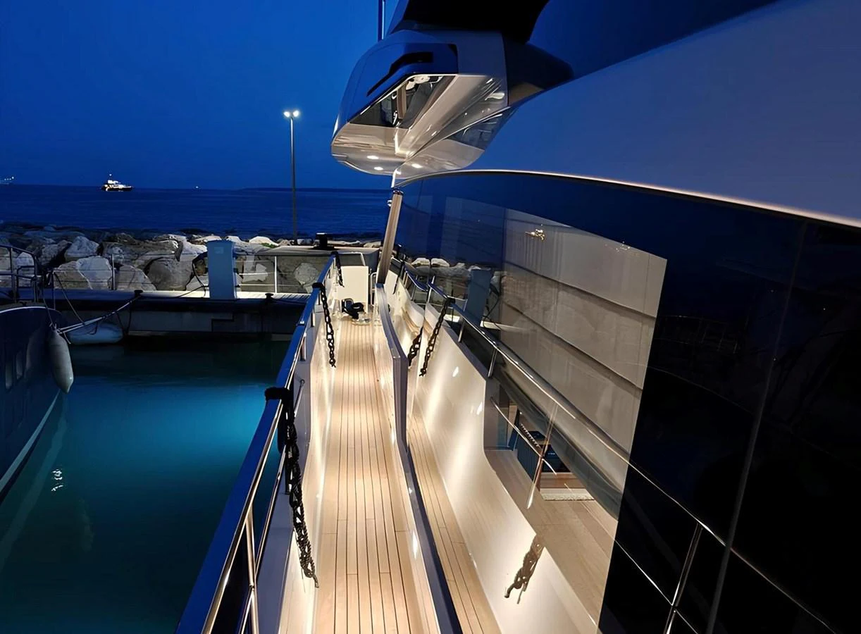 The yacht's side deck is beautifully illuminated against a serene evening backdrop. aboard NADINKA Yacht for Sale