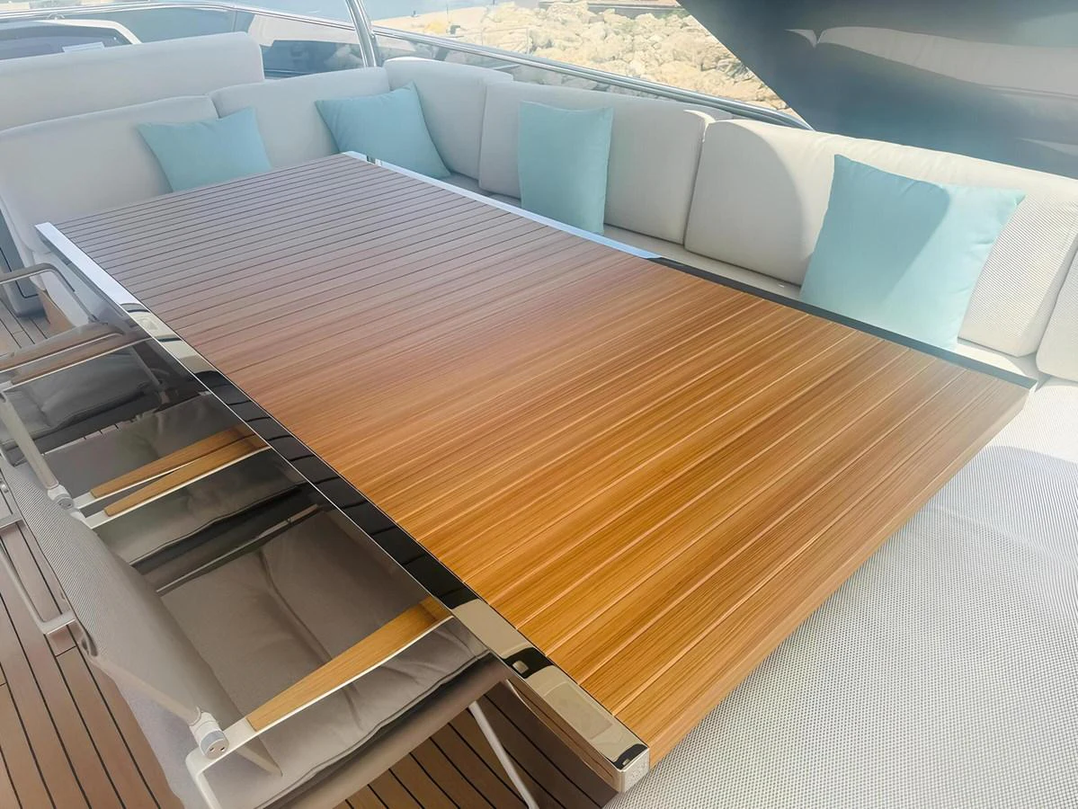 The yacht features a stylish outdoor dining area with a sleek wooden table and comfortable seating adorned with light blue cushions. aboard NADINKA Yacht for Sale