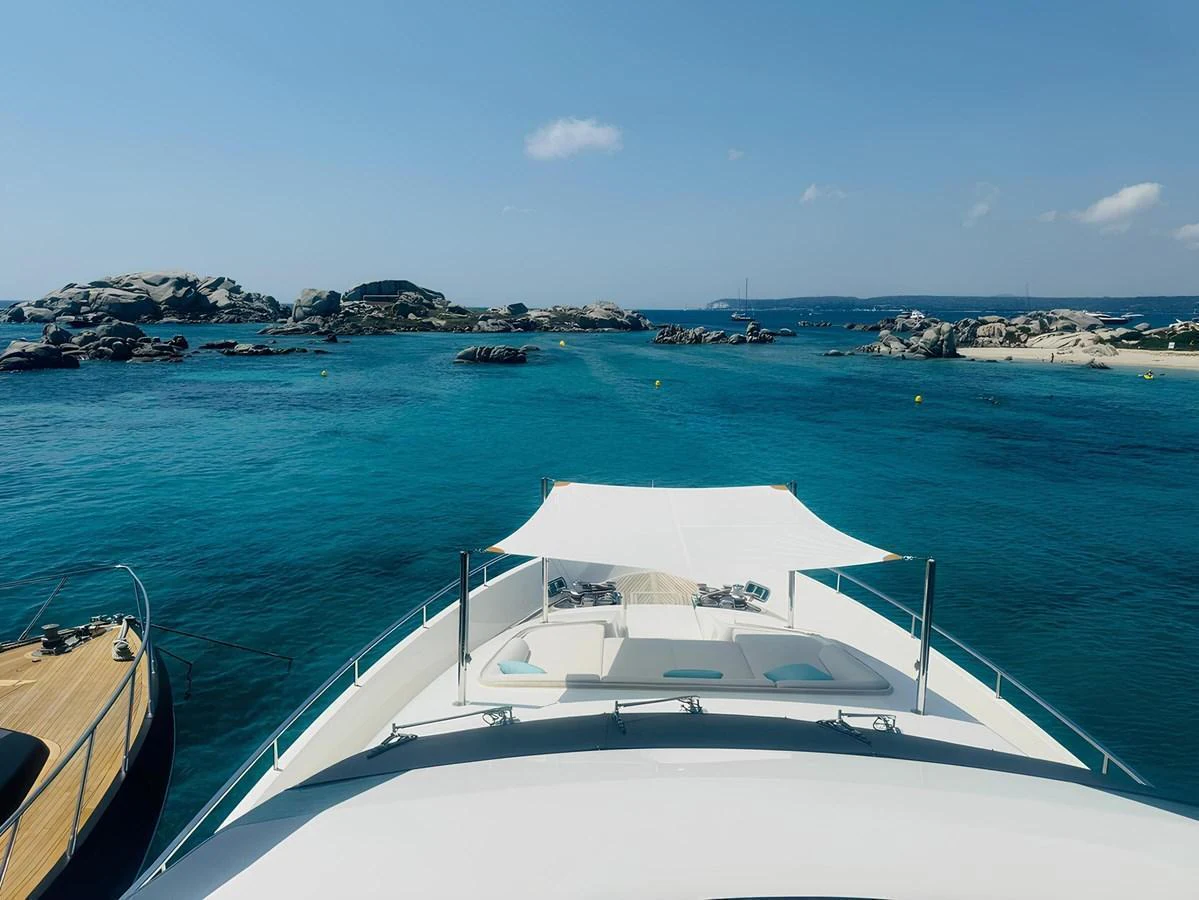 The yacht's bow offers a serene view of turquoise waters and rocky islets under a clear blue sky. aboard NADINKA Yacht for Sale