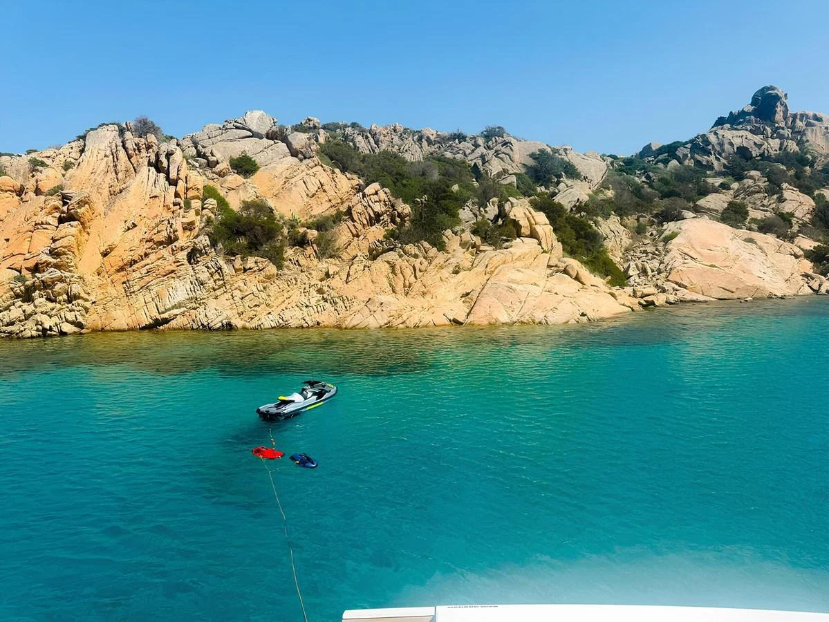 A tender floats serenely in crystal-clear turquoise waters near a rocky shoreline. aboard NADINKA Yacht for Sale
