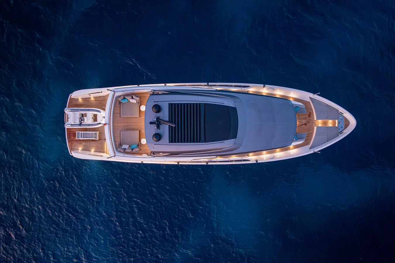 An elegant yacht is captured from above, showcasing its sleek design and ambient lighting against the deep blue water. aboard SANLORENZO SX 88 M&M Yacht for Sale