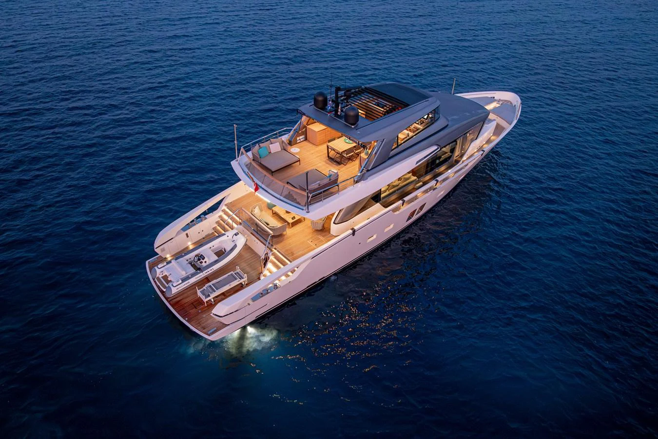 A luxurious yacht cruising on calm waters at dusk, showcasing its elegant aft deck and upper deck lounge areas. aboard SANLORENZO SX 88 M&M Yacht for Sale