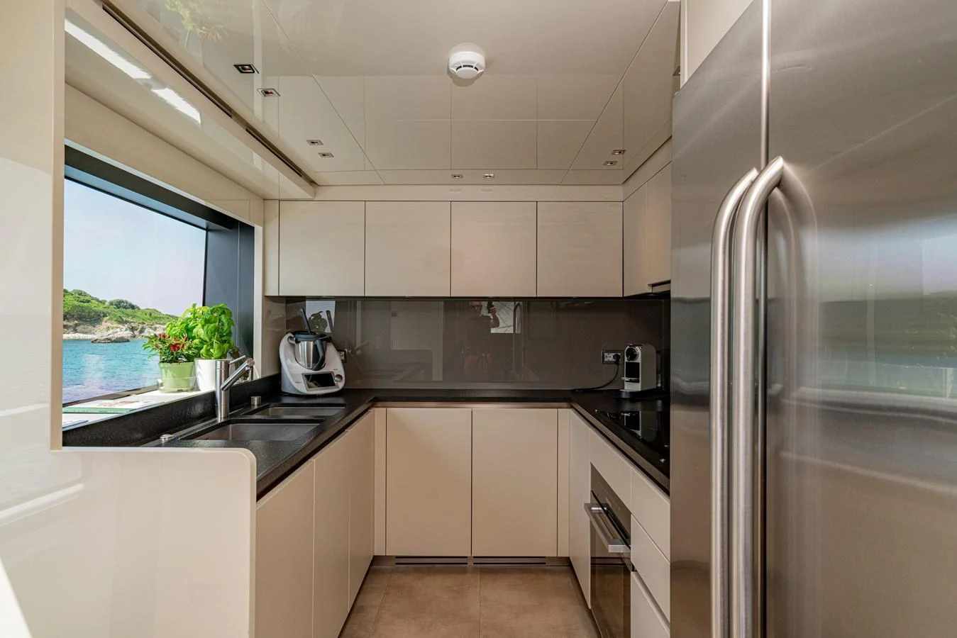 The yacht's galley is modern and well-equipped, featuring sleek cabinetry and stainless steel appliances with a view of the sea through a large window. aboard SANLORENZO SX 88 M&M Yacht for Sale
