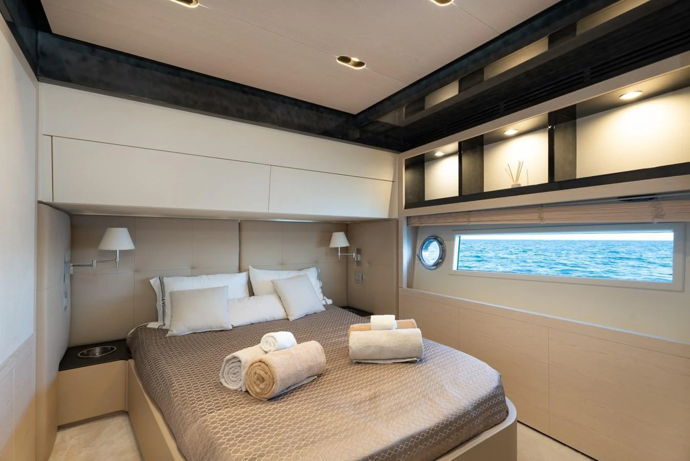 A luxurious stateroom with a large bed, modern lighting, and an ocean view through a porthole window. aboard TRINIDAD Yacht for Sale