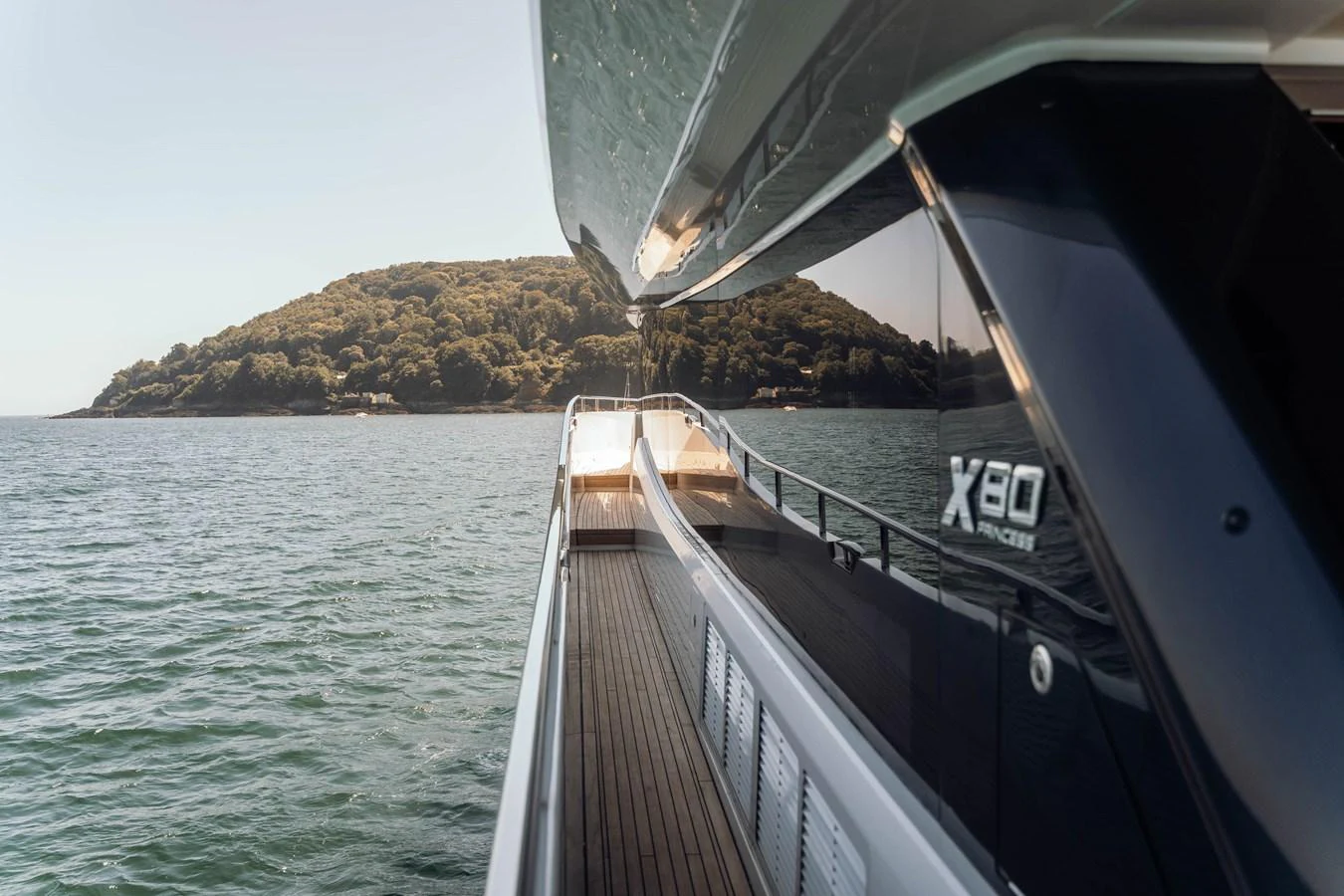 A sleek yacht cruising along the water with a scenic island in the background. aboard CHASE Yacht for Sale