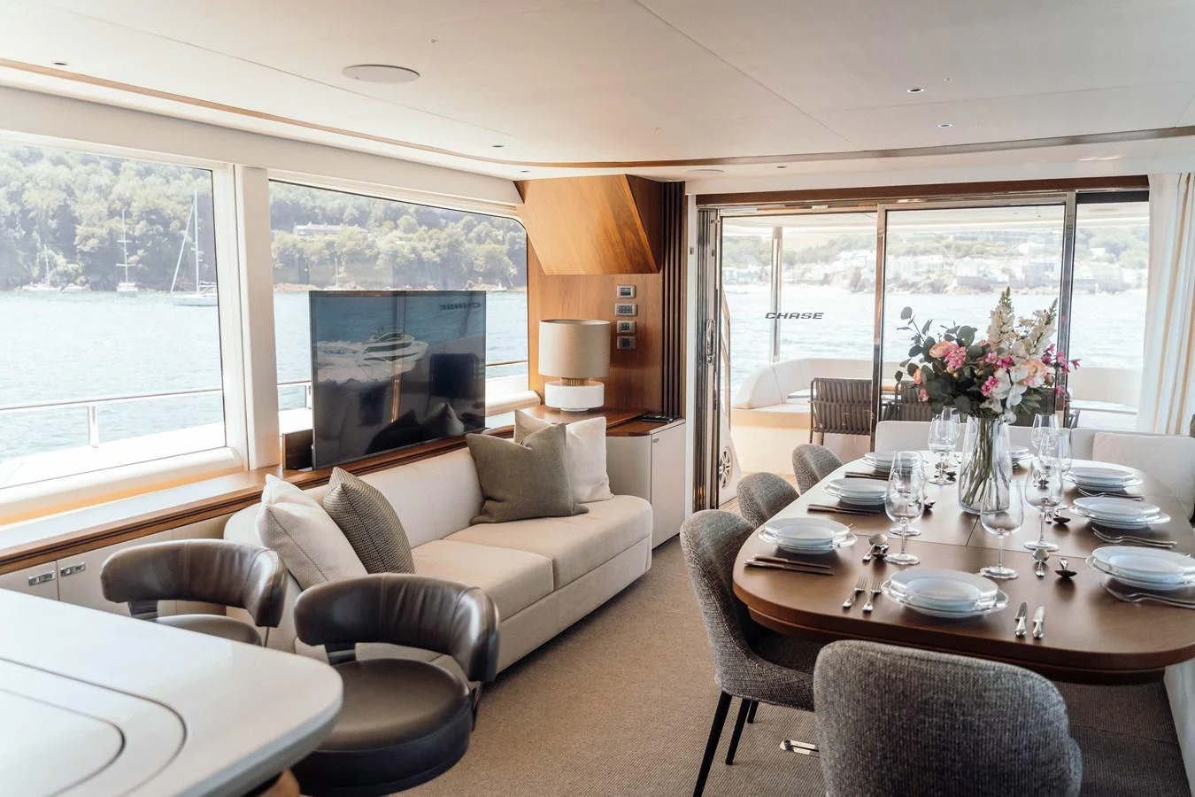 The salon features a comfortable seating area and a dining table with a view of the water through large windows. aboard CHASE Yacht for Sale