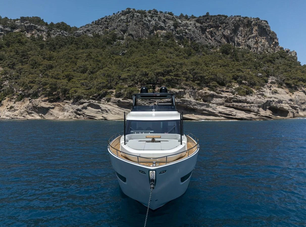 A sleek yacht is anchored in a serene bay with a rocky and forested backdrop. aboard ORCA I Yacht for Sale