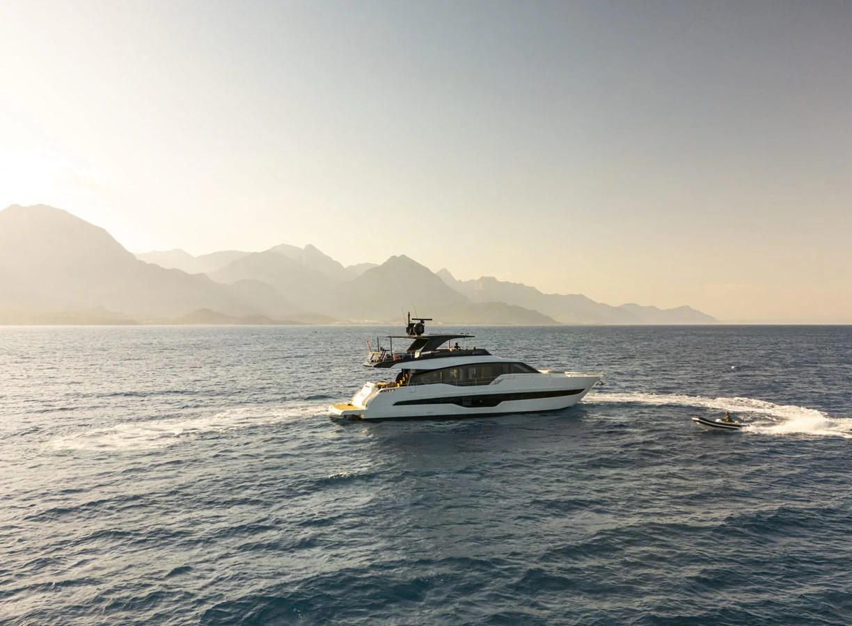 A sleek yacht cruises through calm waters against a backdrop of majestic mountains. aboard ORCA I Yacht for Sale