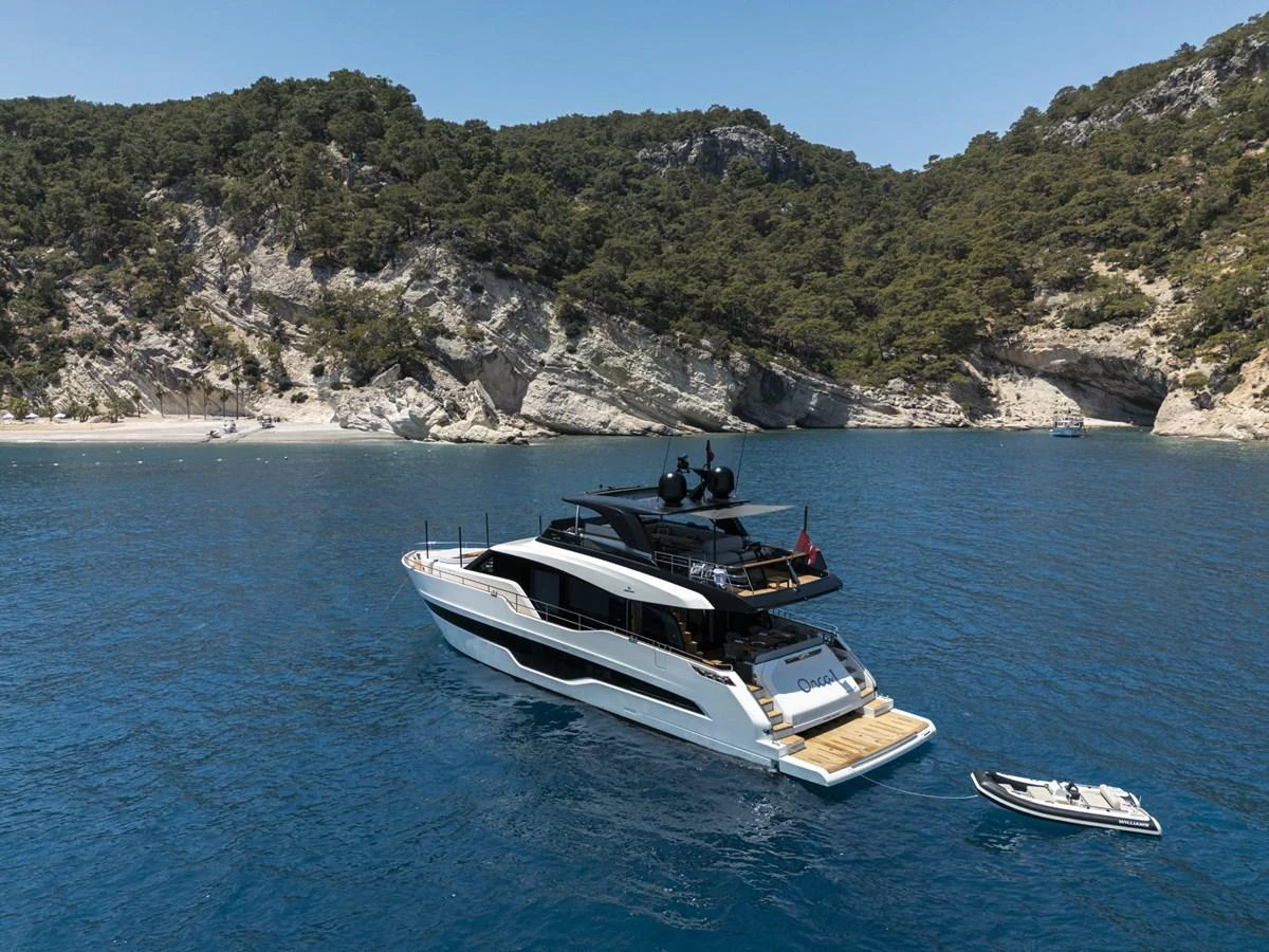 A sleek yacht is anchored in a serene bay with a tender floating nearby. aboard ORCA I Yacht for Sale