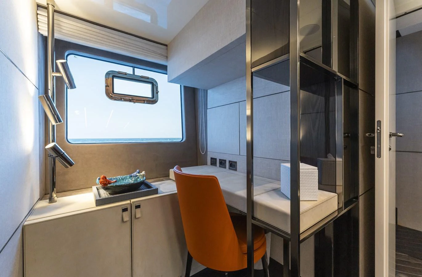A modern yacht office with a sleek desk, an orange chair, and a large window offering a view of the sea. aboard ORCA I Yacht for Sale