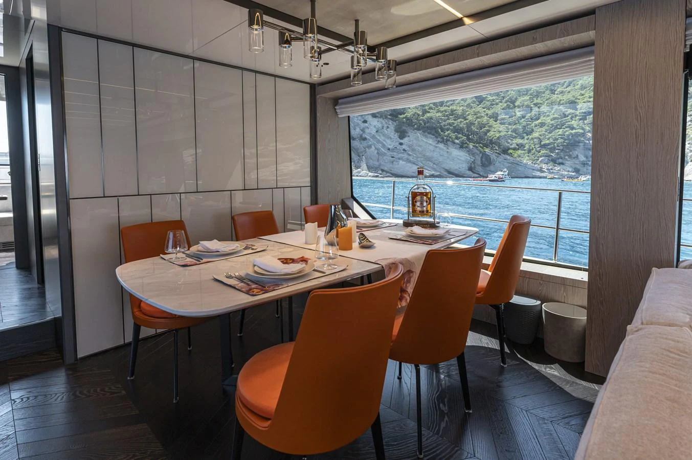 The yacht's dining area features a stylish table with orange chairs and a scenic view through large windows. aboard ORCA I Yacht for Sale
