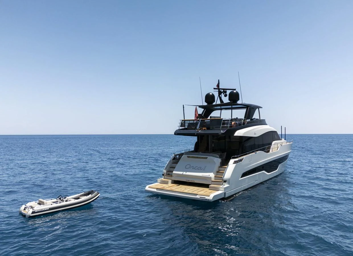 A sleek and modern yacht is anchored in calm blue waters, accompanied by a tender boat. aboard ORCA I Yacht for Sale