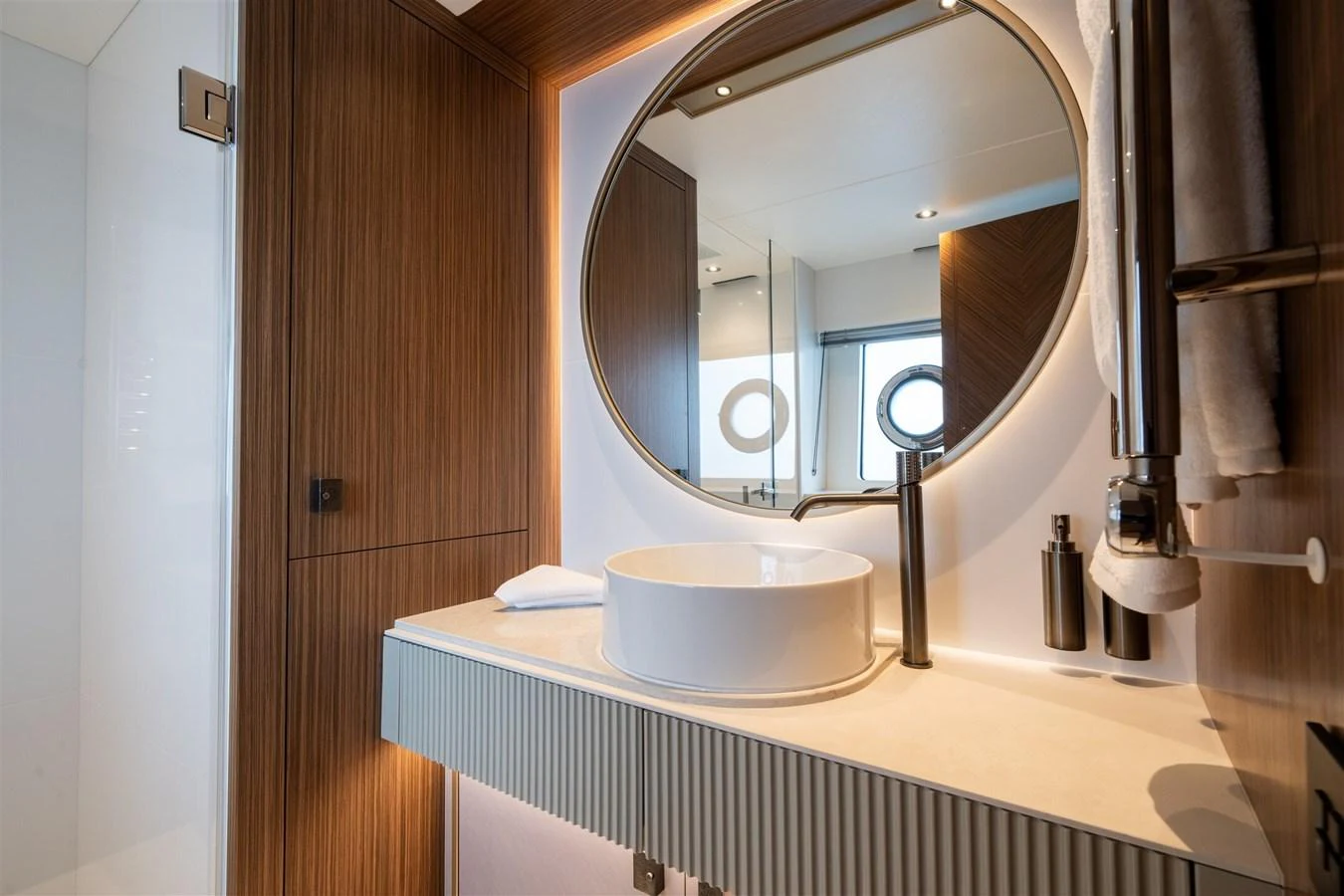 A modern yacht bathroom featuring a sleek round mirror and elegant fixtures. aboard 82 OCEAN ENCLOSED Yacht for Sale