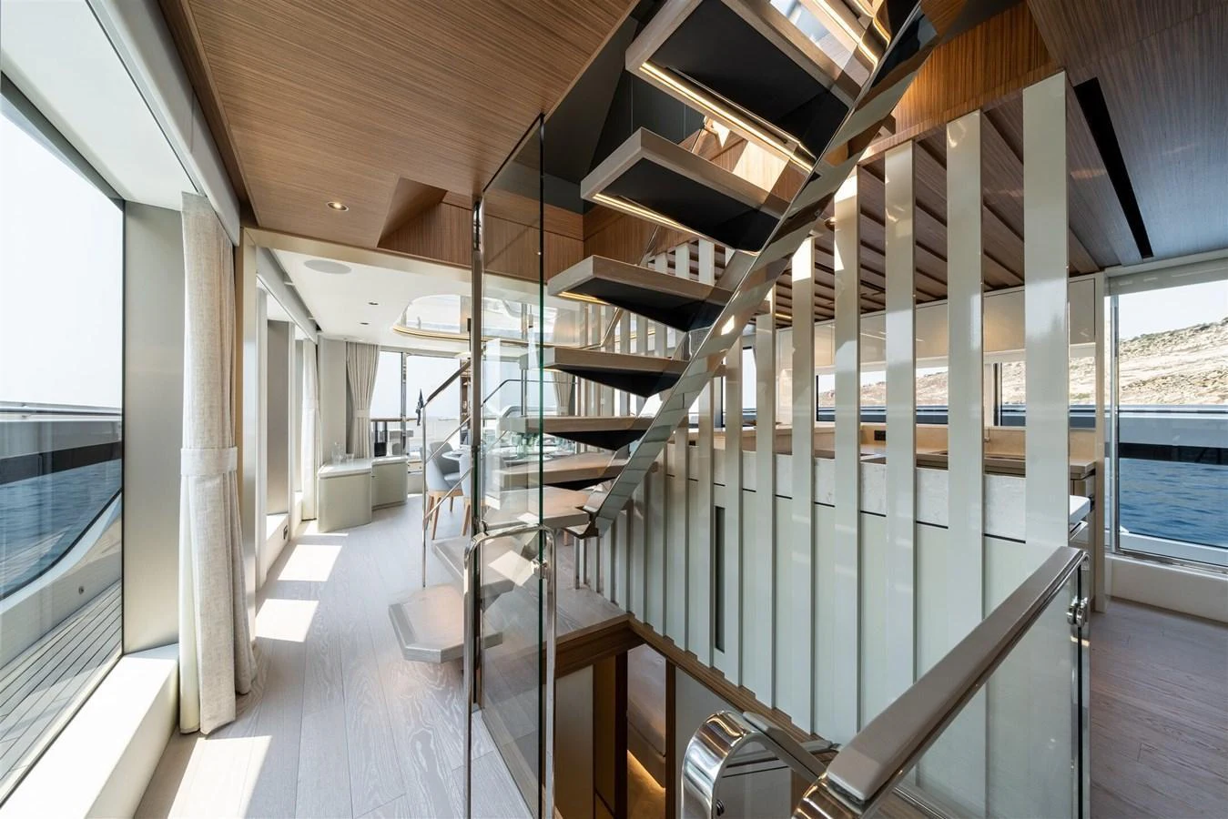 A modern and elegant staircase with glass railings and wooden steps, surrounded by large windows offering stunning sea views. aboard 82 OCEAN ENCLOSED Yacht for Sale