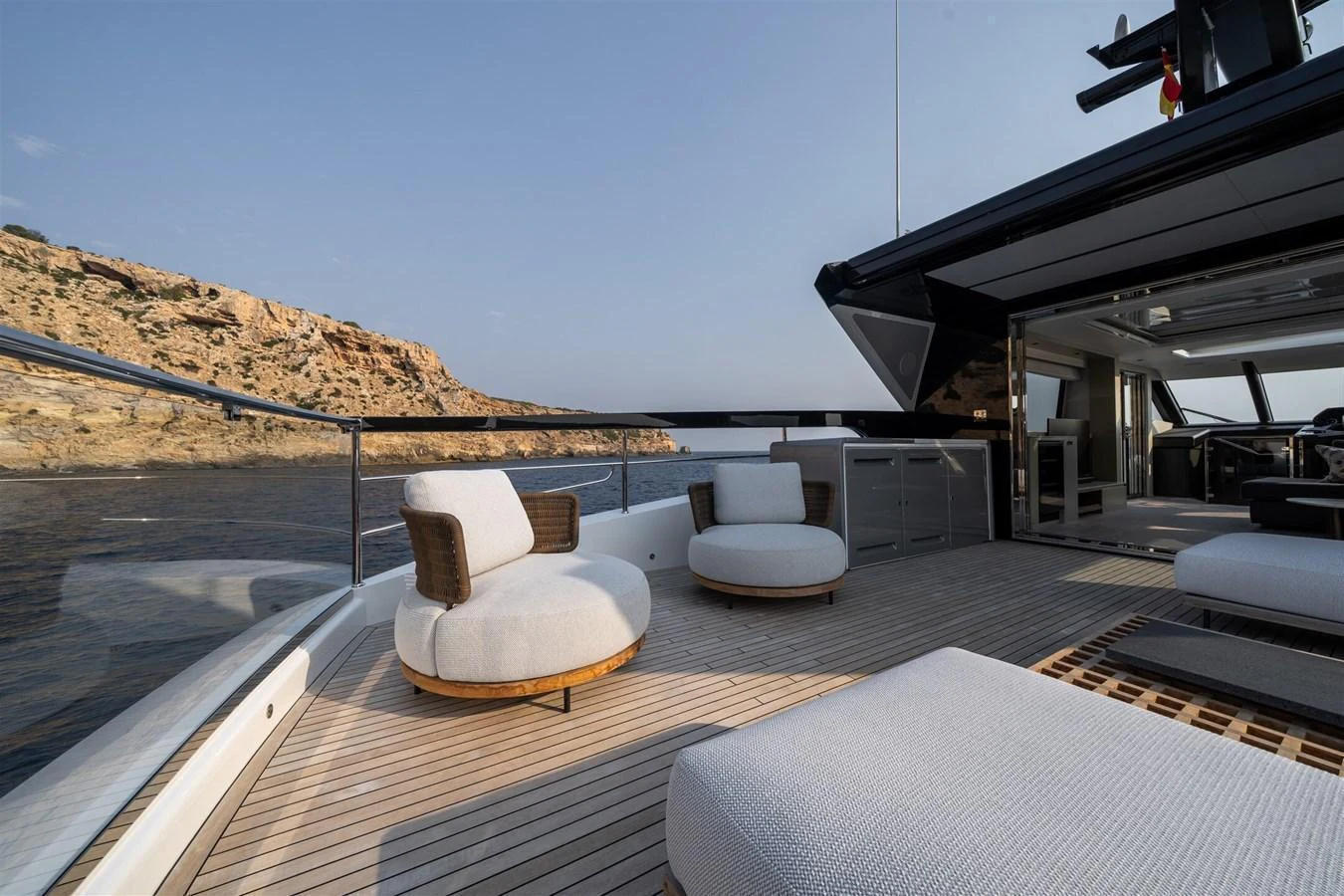 The aft deck features stylish outdoor seating with a scenic view of the coastline. aboard 82 OCEAN ENCLOSED Yacht for Sale