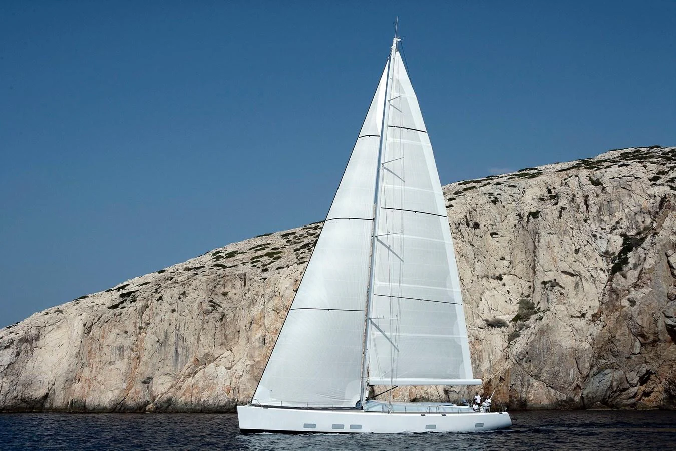 A sleek sailing yacht glides gracefully against a rocky coastal backdrop. aboard POLYTROPON II Yacht for Sale