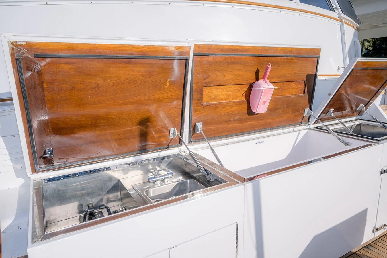 The image showcases a detailed view of the yacht's outdoor storage compartments with wooden lids and a pink dustpan hanging inside. aboard MAMA BEAR Yacht for Sale
