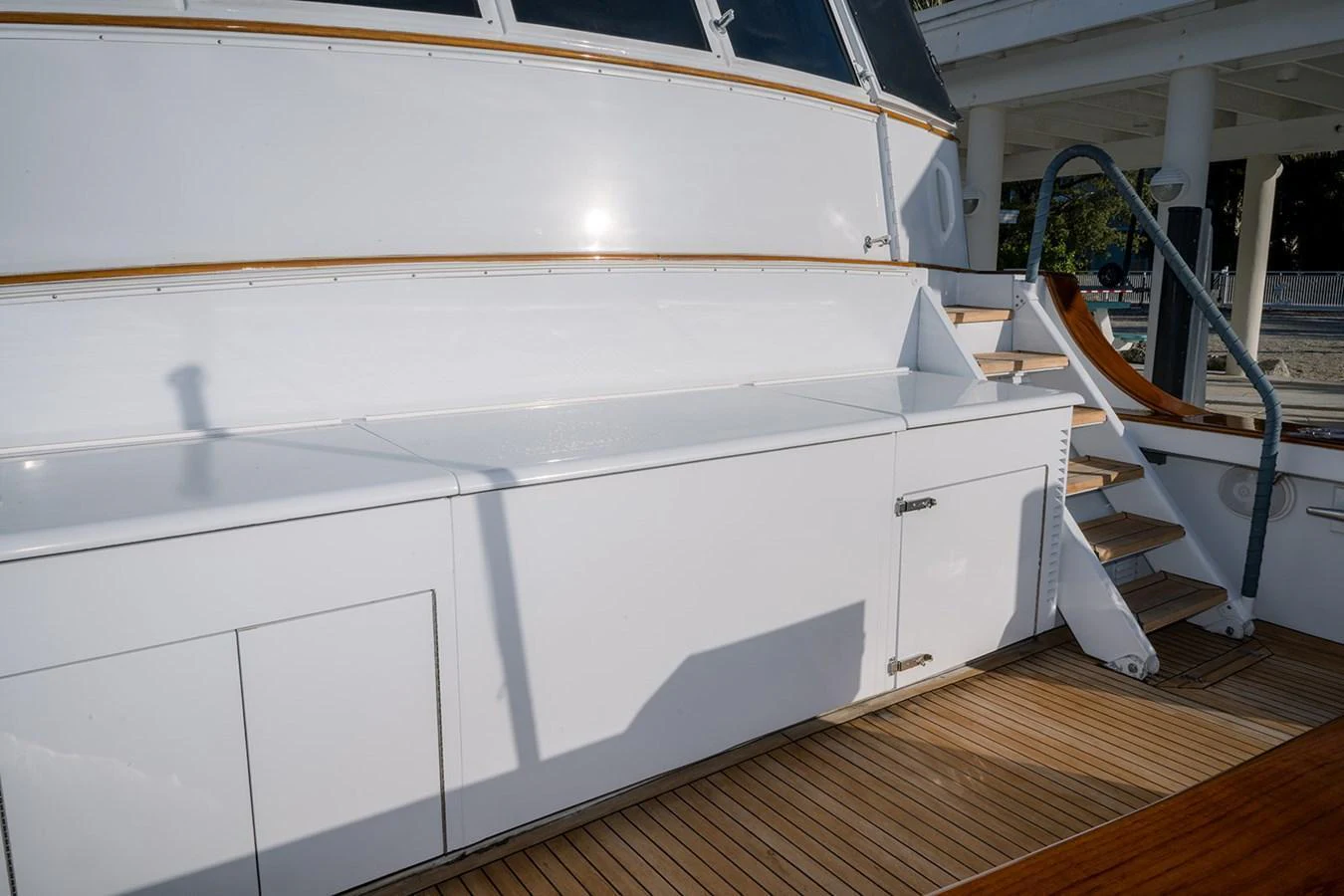 The yacht's deck features sleek white cabinetry and wooden steps leading to an upper level. aboard MAMA BEAR Yacht for Sale