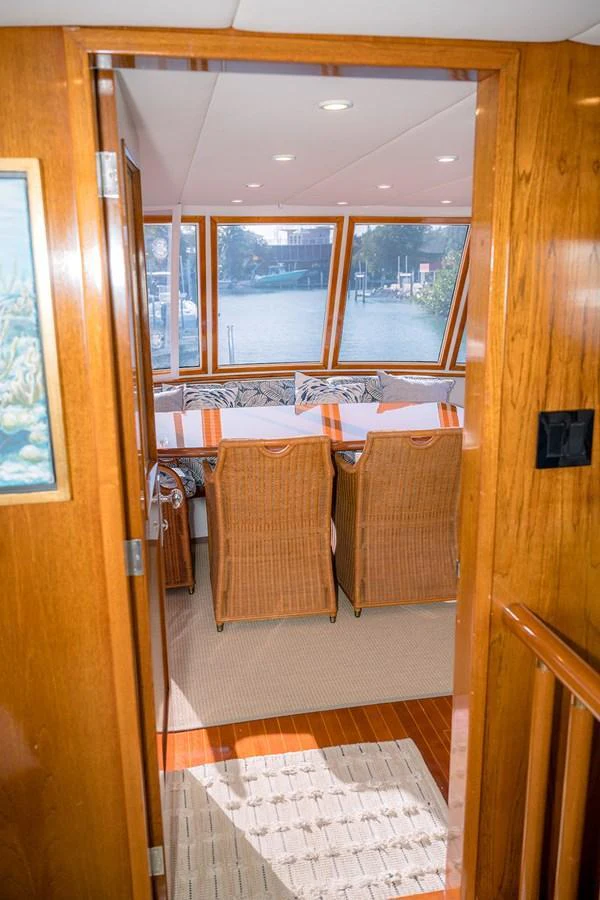 The image showcases a cozy dining area with wicker chairs and a large window providing a scenic view. aboard MAMA BEAR Yacht for Sale