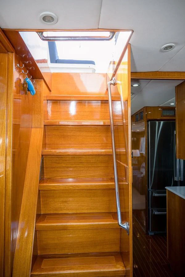 A wooden staircase leads to the upper deck of the yacht, with a glimpse of the galley area in the background. aboard MAMA BEAR Yacht for Sale