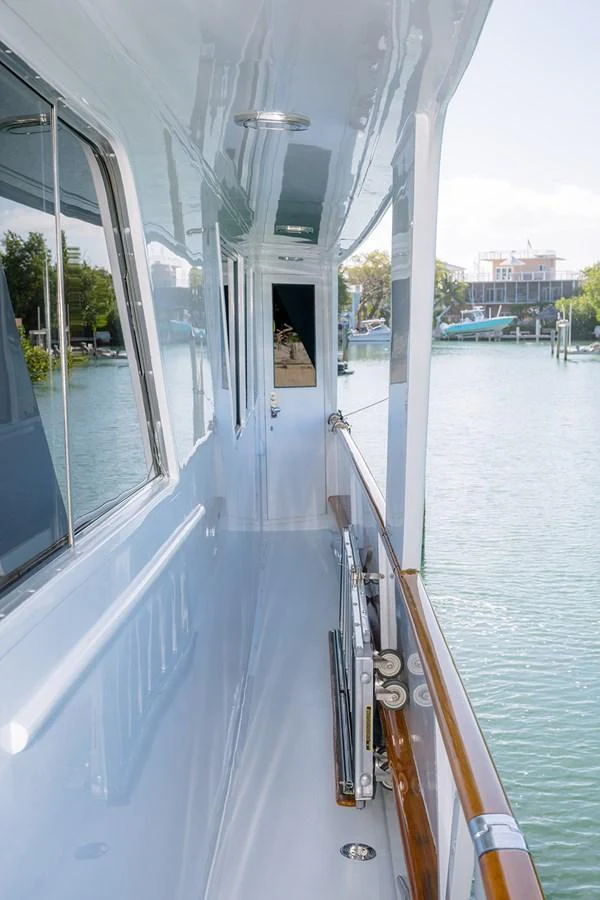 The yacht's side deck offers a sleek walkway with a polished handrail and a view of the serene waters. aboard MAMA BEAR Yacht for Sale