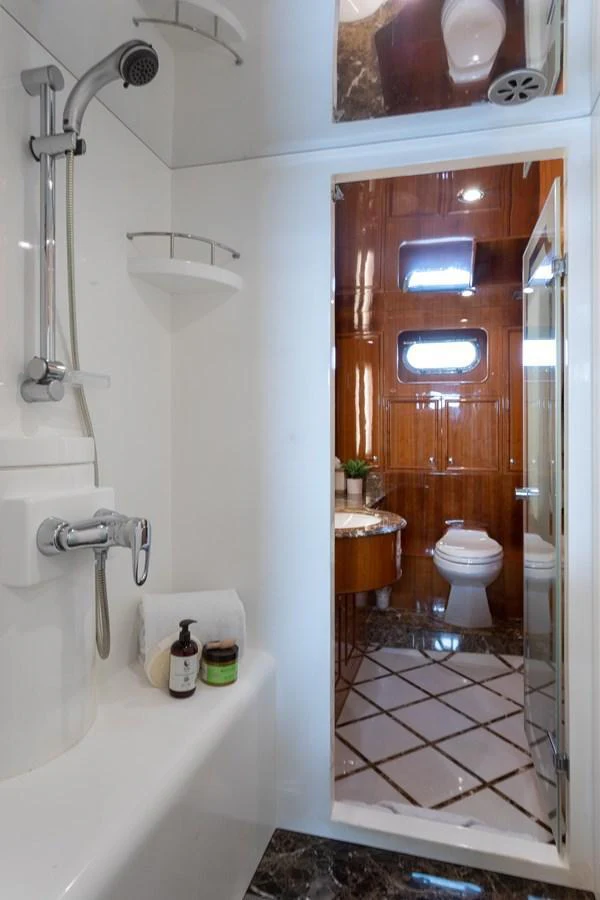 A well-appointed yacht bathroom featuring a shower and a view into the toilet area with wooden accents. aboard PRIME TIME Yacht for Sale