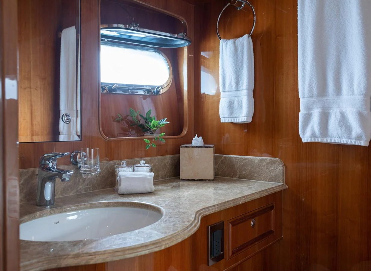 The yacht's bathroom features elegant wood paneling and a marble countertop, complemented by plush white towels and a small window for natural light. aboard PRIME TIME Yacht for Sale