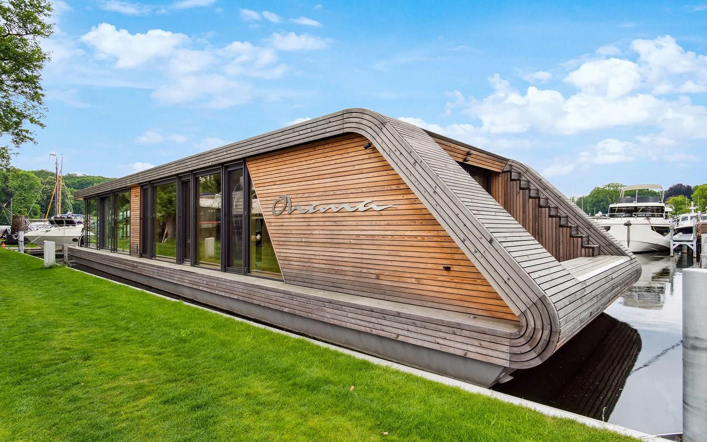 A modern houseboat with sleek wooden paneling docked by the marina. aboard OHANA Yacht for Sale