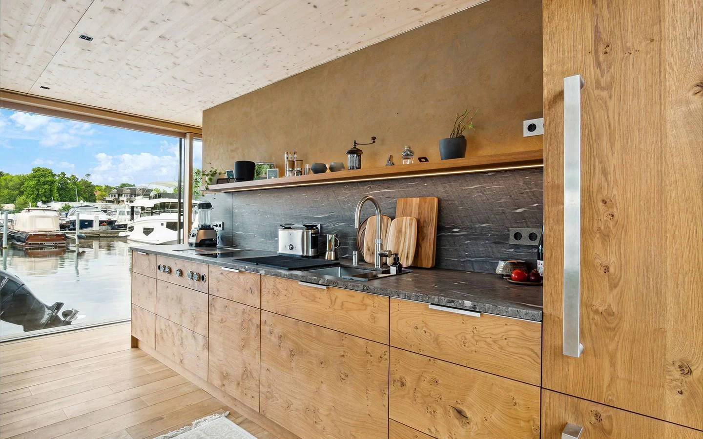 A modern galley with wooden cabinetry and a view of the marina through large windows. aboard OHANA Yacht for Sale