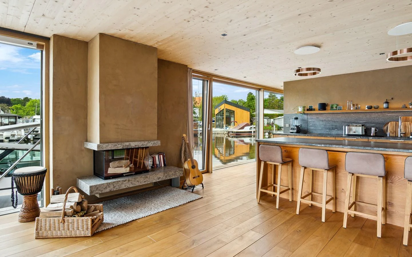 The salon features a cozy fireplace, a guitar, and a modern kitchen area with bar seating, all bathed in natural light from large windows. aboard OHANA Yacht for Sale