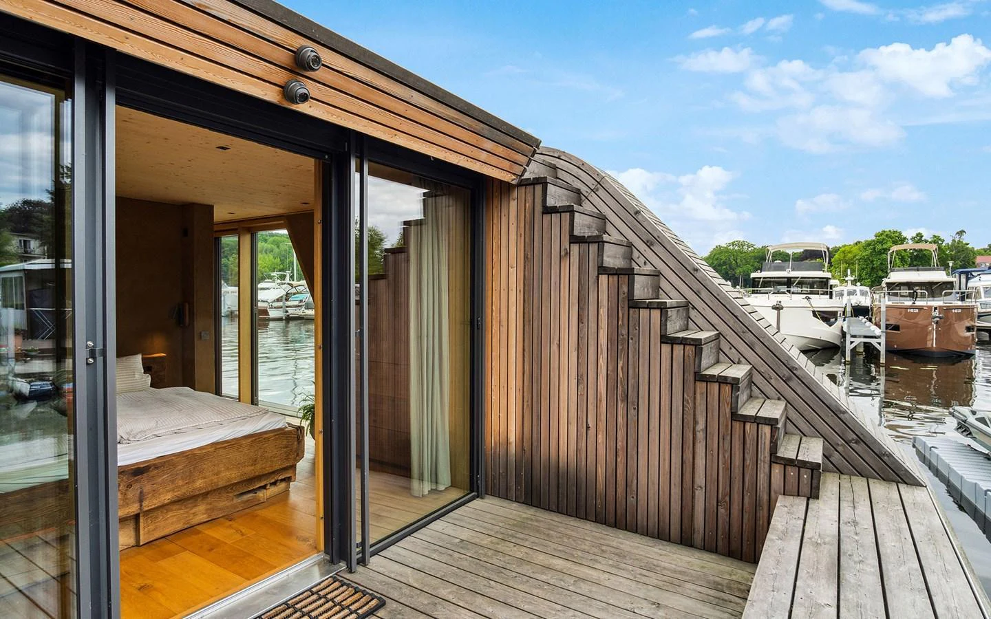 A stylish wooden deck area with an adjacent bedroom, overlooking a serene marina. aboard OHANA Yacht for Sale