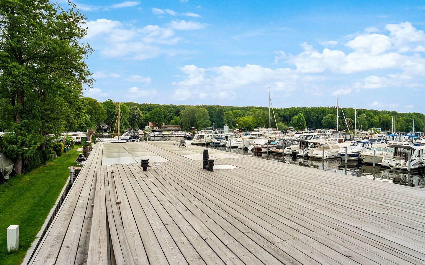 A serene marina with multiple yachts docked, surrounded by lush greenery and calm waters. aboard OHANA Yacht for Sale
