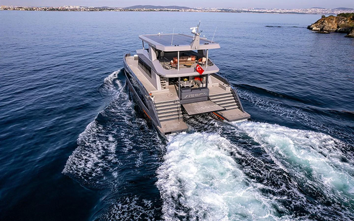 A sleek and modern yacht cruising through calm waters with a scenic coastal backdrop. aboard SITARA Yacht for Sale