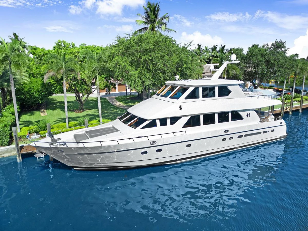A sleek, modern yacht is docked in a serene, tropical marina with lush greenery in the background. aboard SUE CAROLYN Yacht for Sale