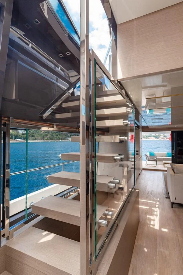 A modern staircase with glass railings leads to a bright and airy interior space with a view of the water. aboard REGINE OF CANNES Yacht for Sale